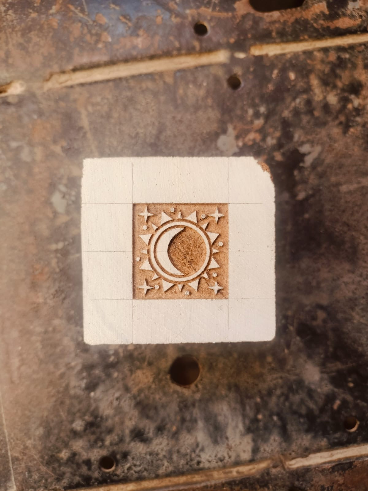 Wooden stamp with a moon and star design on a white square background, placed on a textured metal surface.